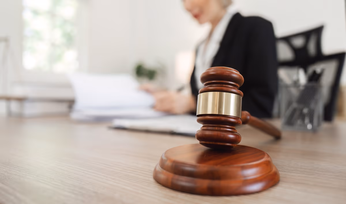 A wooden gavel on a desk with an attorney in the background