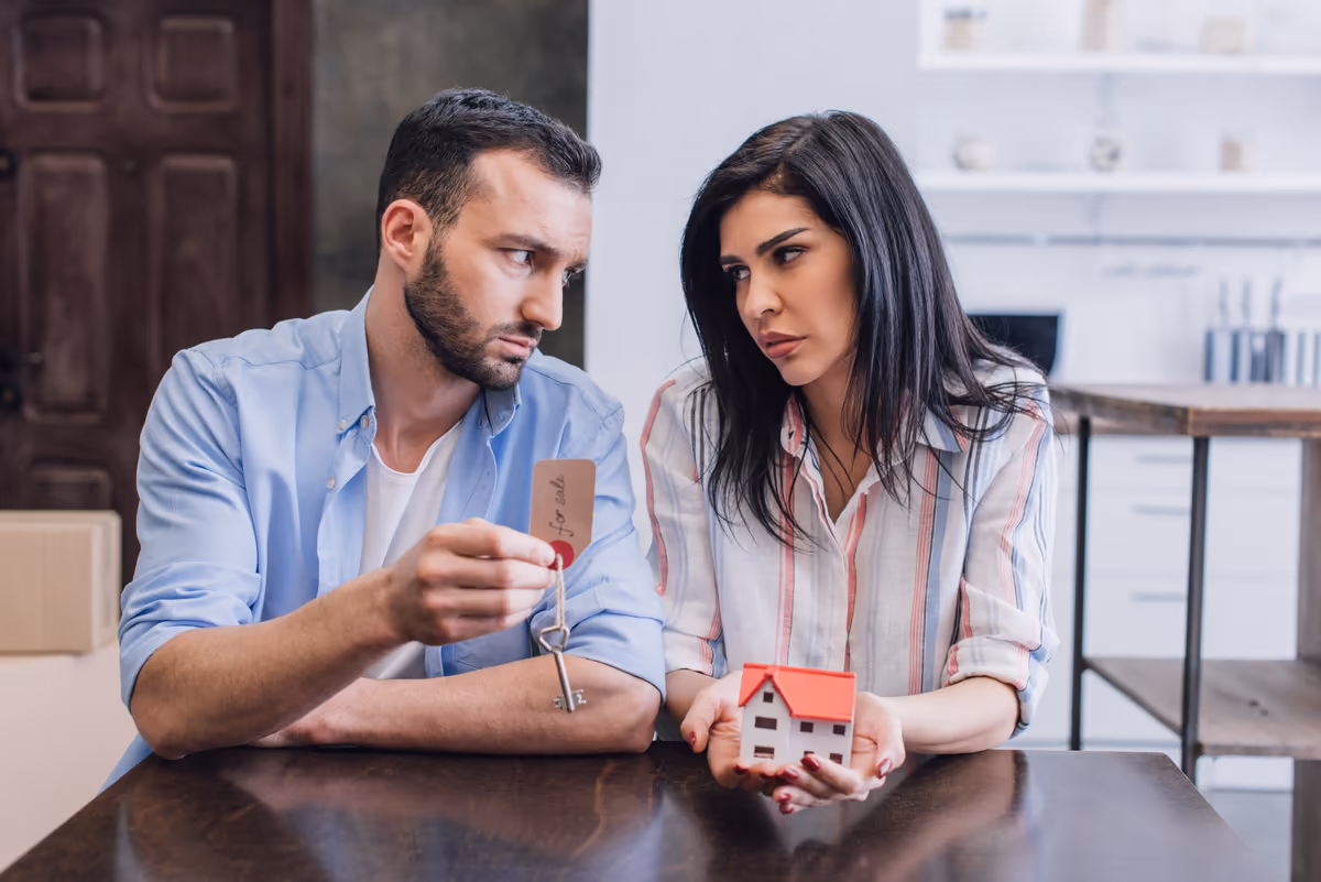 A couple at a table holding a model house and a house key