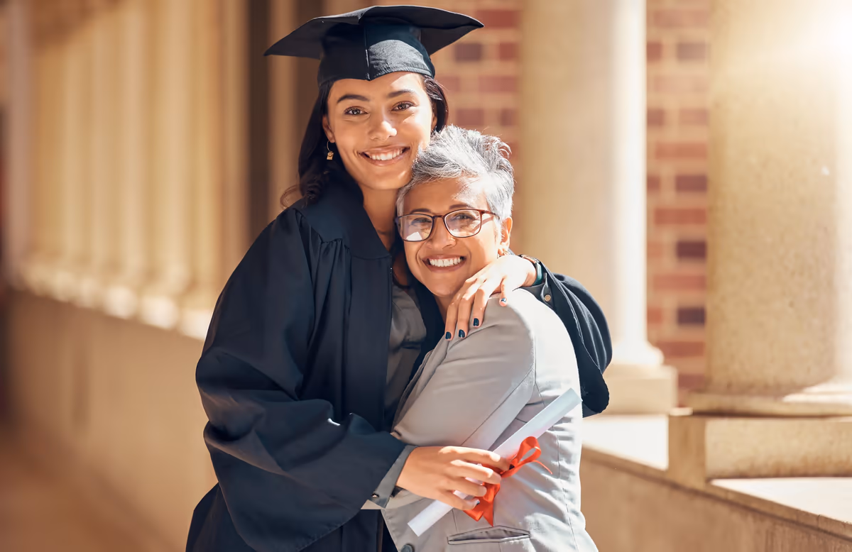 A graduate in cap and gown hugging her mother